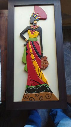 a woman in a colorful dress is holding up a framed art piece