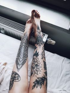 a woman's legs with tattoos on them sitting on a white bed next to a heater