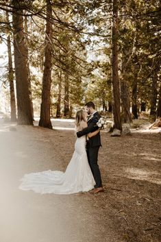 a bride and groom standing in the middle of a wooded area with trees behind them