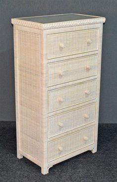 a white wicker dresser with four drawers and glass top on the bottom drawer, against a gray wall