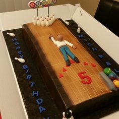 a birthday cake that is decorated with bowling pins and a man laying on the ground