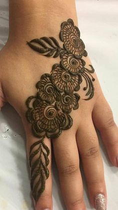 a woman's hand with henna tattoos on her left hand and flowers painted on it