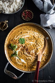 a pan filled with curry and rice on top of a wooden table next to other dishes