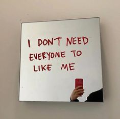 a person holding a cell phone in front of a mirror with writing on it that says, i don't need everyone to like me