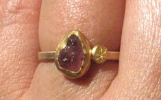 Natural rough dark pink Tourmaline (about 8 x 6 mm), Is wrapped in 22k solid yellow gold with a 22k gold stamped disc on one side. It all rests on a flat 9k solid yellow gold band, about 1.5 mm wide and 1 mm thick. Matte finish. This ring size is a 6. Can be enlarged a bit. READY TO SHIP! In a gift box. Handmade Tourmaline Gold Ring, Handmade Gold Tourmaline Ring, Rough Stone Ring, Stackable Engagement Ring, Gold Rings Stackable, Tourmaline Ring, Yellow Gold Ring, 22k Gold, Gold Band