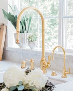 a kitchen sink with gold faucets and white flowers