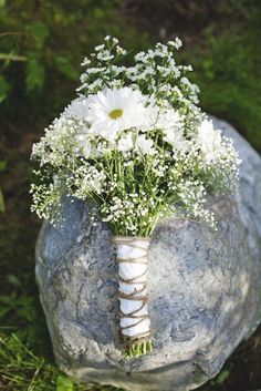 a bouquet of white flowers sitting on top of a rock in front of some grass