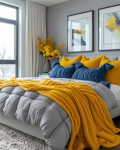 a bed with yellow and blue pillows in a bedroom next to two large pictures on the wall