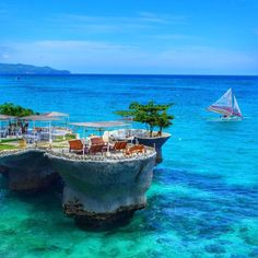 an island in the middle of the ocean with chairs and umbrellas on it's edge