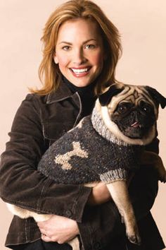 a woman holding a pug wearing a sweater