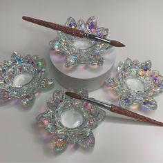 three crystal candlestick holders with glittered lids and brushes in them on a white surface