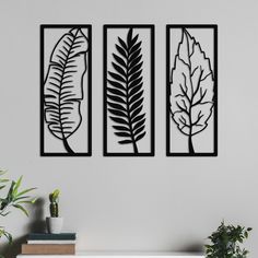 three metal wall art pieces hanging on a white wall next to a potted plant