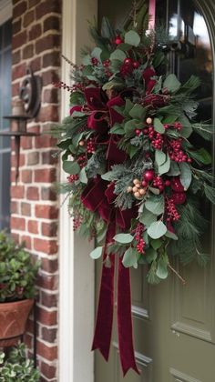 a wreath hanging on the front door of a house decorated with greenery and berries