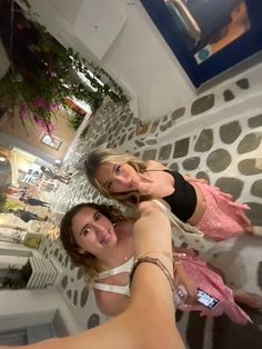 two beautiful young women taking a selfie in front of a stone wall with potted plants