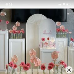 pink flowers are in vases on a table next to white cabinets and a mirror