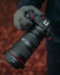 a person holding a camera in their right hand and wearing gloves on top of it