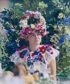 a woman sitting at a table with flowers on her head and fruit in front of her