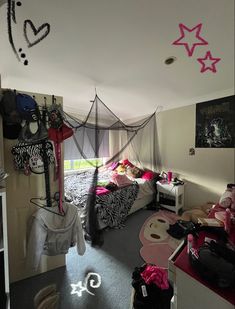 a bedroom with pink and black decorations on the ceiling, bed in the corner and other items hanging from the ceiling