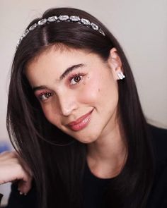 a woman with long dark hair wearing a tiara and smiling at the camera,