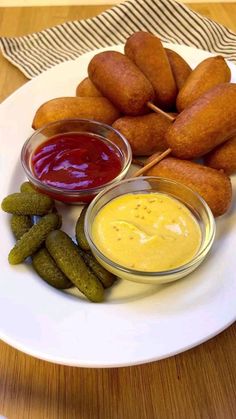 a white plate topped with fried food and dipping sauces next to pickle sticks