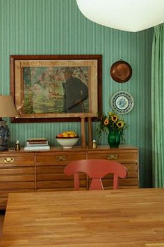 a dining room with green wallpaper and wooden table in front of a painting on the wall