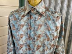 This 90's vintage shirt has the perfect retro vibes. A long sleeve, collard shirt in light blue with an all over paisley design. Crafted from a woven poly fabric that adds a hint of shimmer. A fun piece to pair with a suit or dress down with jeans or slacks.  Size Medium Measurements: Chest: 114 cm / 45 inches Shoulder: 51 cm / 20 inches Length: 82.5 cm / 32.5 inches Sleeve: 60.5 cm / 23.75 inches 100% Polyester This item is one of a kind. BUYING VINTAGE: While all care is taken to state any obvious faults, please note that when you buy a vintage or preloved item, they may show small signs of ageing, wear and/or repair. Visit my website   https://phoenixmenswear.com.au/ Lots of fun stuff for guys and girls...!! Please note that if you are ordering from anywhere outside of Australia please Blue Paisley Print Long Sleeve Shirt, Classic Blue Paisley Print Tops, Fitted Tops With Paisley Print And Spread Collar, Fitted Paisley Print Top With Spread Collar, Fitted Light Blue Shirt For Fall, Fitted Collared Shirt With Paisley Print, Blue Long Sleeve Shirt With Vintage Print, Vintage Fitted Patterned Shirt, Fitted Vintage Patterned Shirt