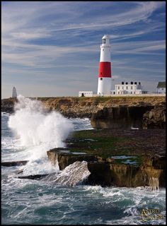 a lighthouse on top of a cliff next to the ocean with waves crashing against it