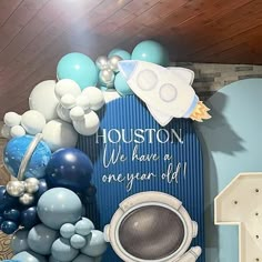 a blue and white backdrop with balloons, an infant's first birthday sign and other items