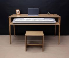 an electronic keyboard sitting on top of a wooden desk next to a small table with a laptop