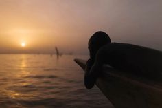 a person sitting on a bench looking out at the ocean with people in the distance