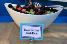 a white bowl filled with blackberries and grapes on top of a table next to a fork