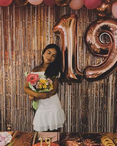 a woman standing in front of a table with balloons and flowers on it, holding a bouquet