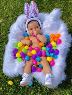 a baby is dressed in an easter bunny costume while laying on the grass with eggs