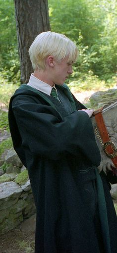 a young man dressed in medieval garb and holding a large book while standing next to a tree