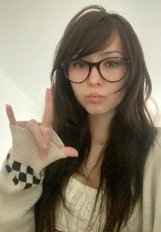 a young woman wearing glasses making the peace sign with her hand while standing in front of a white wall