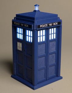 a blue police box is shown on a gray surface with light coming from it's top