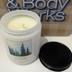 a white candle sitting next to a box with a black lid on it and a cardboard box in the background