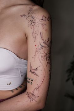 a woman's arm with flowers and birds on her left arm, behind her is a white tank top