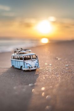 a toy bus sitting on top of a sandy beach next to the ocean at sunset