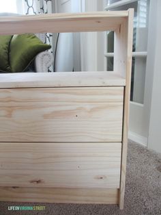 a wooden bed frame with green pillows on top of it and a window in the background