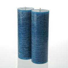 two blue candles sitting next to each other on a white surface with one candle lit