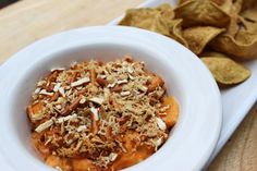 a white bowl filled with food next to some tortilla chips on a plate