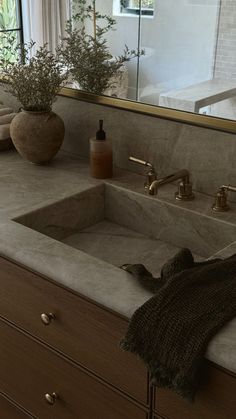 a bathroom sink sitting under a large mirror next to a counter top with two vases on it