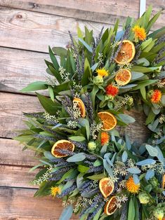 an orange wreath with leaves and flowers on a wooden surface, surrounded by greenery