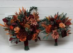 two bridal bouquets with orange and red flowers are on the white wall next to each other