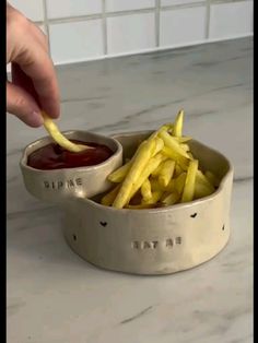 a person dipping fries into a bowl with ketchup and mustard on the side