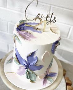 a white cake with purple flowers and the number two on top is sitting on a plate