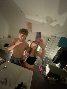 a man and woman taking a selfie in front of a mirror while brushing their teeth