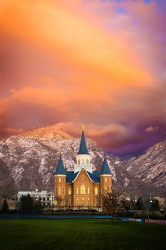 an old church in the mountains under a colorful sky with clouds and snow on top