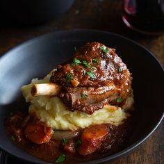 a black bowl filled with meat and mashed potatoes on top of a wooden table